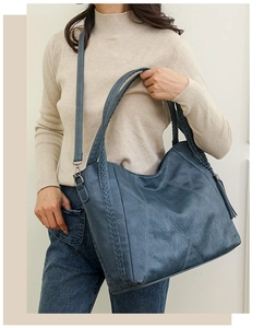 Detail of dark blue leather tote bag with woven handles and tassel on a female model