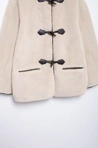 Détail de la texture du manteau en peau de mouton avec boucles en cuir et fourrure crème
