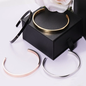 Polished C-shaped stainless steel cuffs in four colors displayed around a black gift box