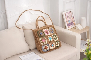 Detail of handmade straw tote bag featuring colorful crochet floral patterns and dual handles