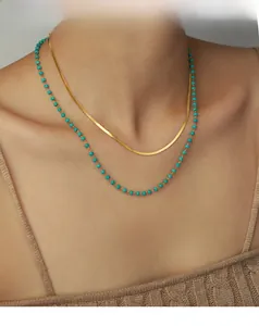 Close-up of layered gold snake chain and turquoise bead necklace on woman neck