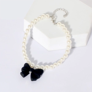 Detailed macro of a pet pearl necklace featuring a black bow pendant on a white stand