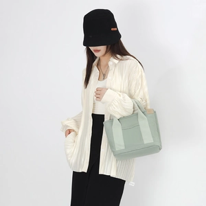 Detail view of light green canvas tote bag with front pocket held by model in casual outfit