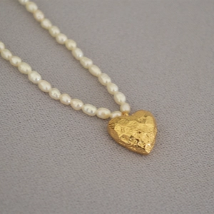 Macro detail of a golden heart pendant with hammer texture on a white freshwater pearl necklace