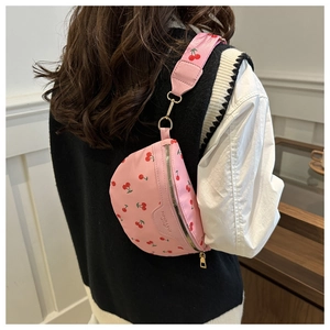 Close-up of pink crossbody bag with cherry pattern and wide strap on model