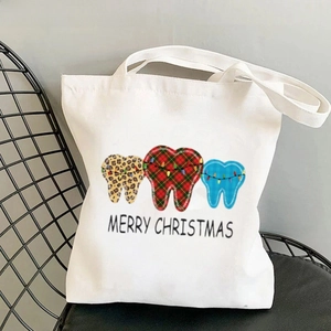 Detail of white canvas tote bag featuring dentist-themed Christmas tooth print on a chair