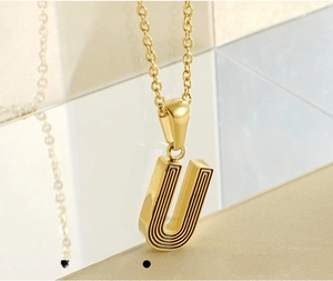 Détail macro du pendentif lettre U en acier inoxydable doré avec rainures gravées