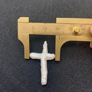 Macro shot of natural white irregular cross pearl being measured with brass calipers