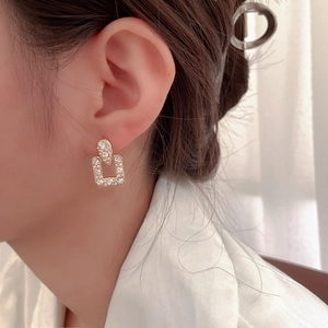Eleganti orecchini geometrici dorati con strass indossati da una modella in luce calda