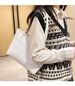 Detailed close-up of white tote bag with crocodile texture worn by model