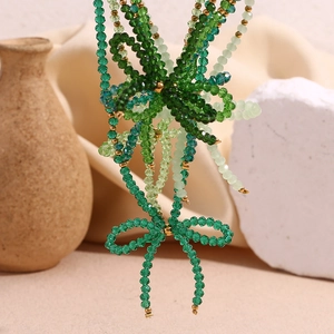 Detail of handmade green faceted crystal beads with a metal bow pendant and gold accents