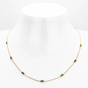 Detail view of gold choker necklace featuring seven emerald-cut green gemstones on box chain