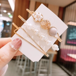 Détail de trois barrettes dorées en perles et strass sur carte tenue à la main