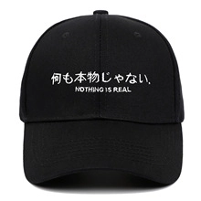 Detail of white embroidery with slogan Nothing Is Real on black cotton baseball cap