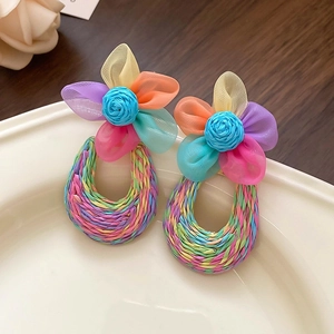 Close-up of vibrant woven floral earrings with colorful petals in a white ceramic dish