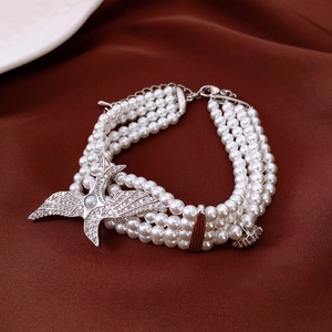 Detail of multi-layer pearl bracelet with silver diamond-encrusted eagle on red fabric