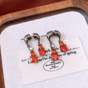 Detailed view of water drop earrings with orange gems and black hooks on wooden tray