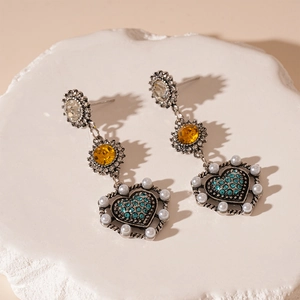 Dettaglio di orecchini vintage con cuore blu, fiori e perle su base di pietra