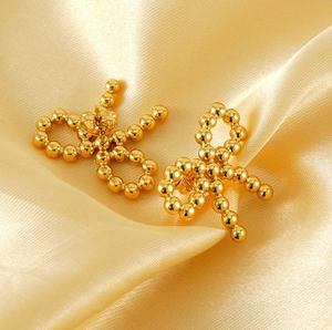 Close-up of golden beaded bow earrings resting on elegant champagne silk fabric