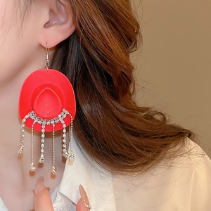 Close-up of red cowboy hat earrings with sparkling rhinestone tassels worn by a model