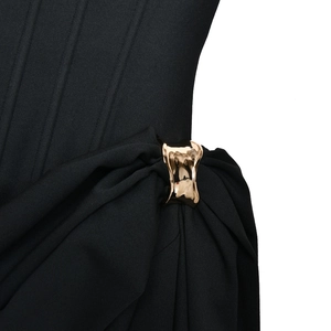 Gros plan d'une robe noire plissée avec une boucle en métal doré de forme irrégulière