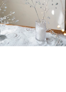 Close-up of sparkling silver branch with crystal drops in a glass vase on a snowy surface