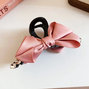 Detailed close-up of a pink satin bow hair claw clip with sparkling rhinestones decoration