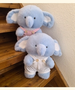 Close-up of plush blue elephant toys wearing corduroy overalls on wooden stairs