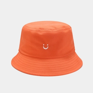 Detail of bright orange bucket hat with white smile face embroidery and twill cotton texture