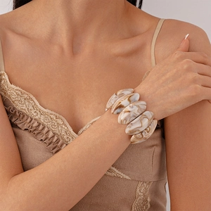 Detail eines breiten, beige-marmorierten Acrylharz-Armreifs am Handgelenk des Models