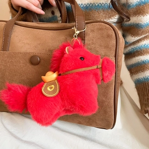 Dettaglio del portachiavi a forma di cavallo di peluche rosso con lingotto d'oro su borsa