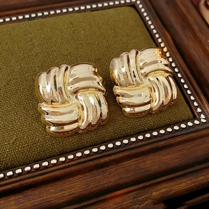 Detail of gold square woven earrings on a green velvet pad showing high-polished texture