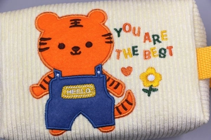 Detailaufnahme der Cord-Textur und Tiger-Stickerei auf einer beigen Kosmetiktasche