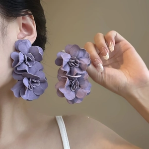 Elegant purple fabric flower earrings with beaded tassels shown on a model