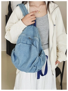 Side view of a light blue denim backpack with zipper pocket and navy straps on a model