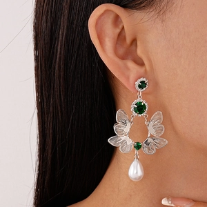 Close-up of butterfly earrings with green crystals and white teardrop pearls on a model