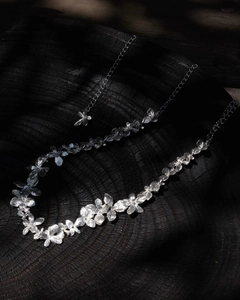 Macro shot of silver floral necklace with matte petal texture on dark wood background