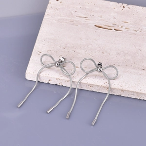 Detail view of silver bow-shaped tassel earrings with snake chain fringe on stone surface