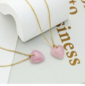 Detail of two gold chains with heart-shaped pink natural stone pendants on aesthetic book