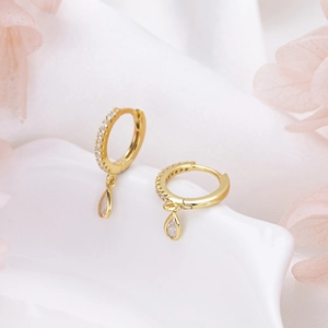 Macro shot of gold hoop earrings with clear teardrop zircon stones on white silk background