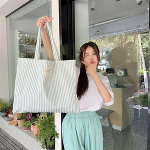 Close-up of light green striped canvas tote bag featuring a minimalist white woven side label