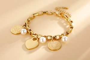 Détail du bracelet chaîne dorée avec pendentif cœur, pièce religieuse et perles blanches