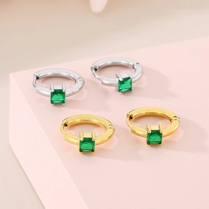 Detail view of gold and silver square emerald earrings on a pink platform