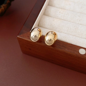 Detail of gold-plated oval stud earrings displayed on a premium wooden jewelry box