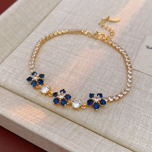 Detailed close-up of blue zircon flower bracelet with gold-plated chain and white accents