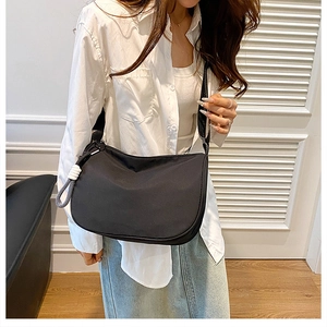 Detail view of black nylon crossbody bag with wide shoulder strap and white charm
