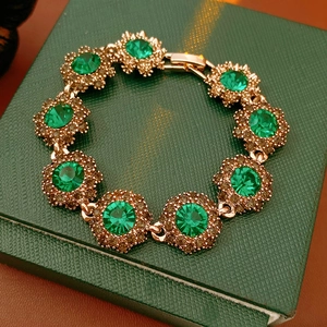 Detailed close-up of emerald style gem bracelet with gold floral clusters in a green box