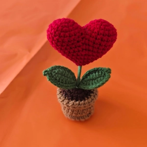 Handmade crochet red heart plant in a brown pot with green leaves on orange background