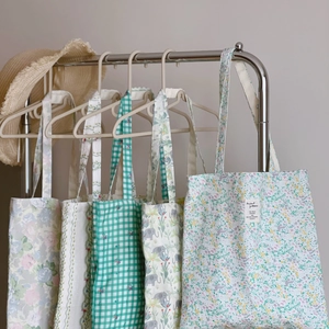Detail of floral and checkered cotton canvas tote bags hanging on a rack with a straw hat