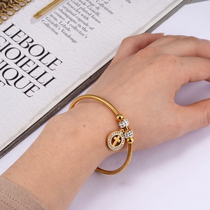 Close-up of golden stainless steel bracelet featuring a crystal-set cross pendant charm
